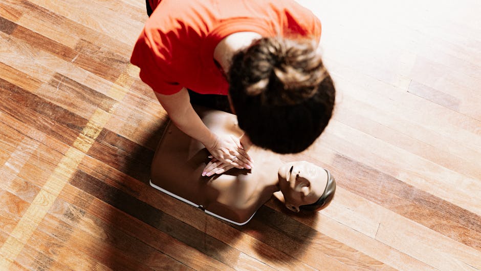 Instructor performs CPR on mannequin during training session on wooden floor.