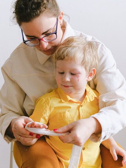A mother attentively applies first aid to her young son indoors.