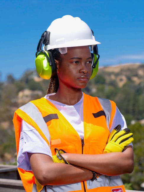 Black woman in PPE outdoors, wearing hard hat and ear protection.