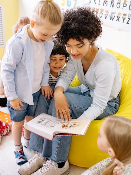 A teacher engaging young children with a storybook in a colorful classroom setting.