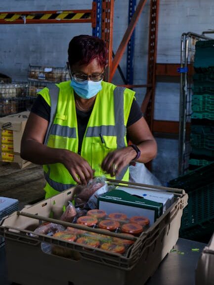 A warehouse worker in safety gear packing food parcels for distribution.