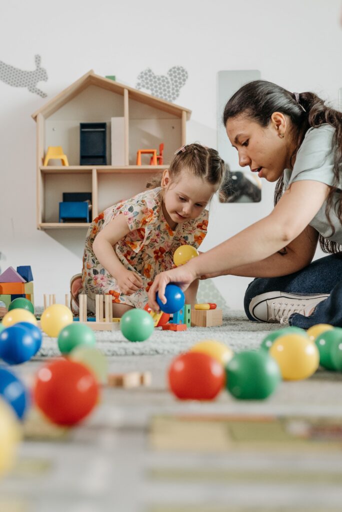 Home A woman and a child playing with colorful balls and blocks in a kindergarten setting.
